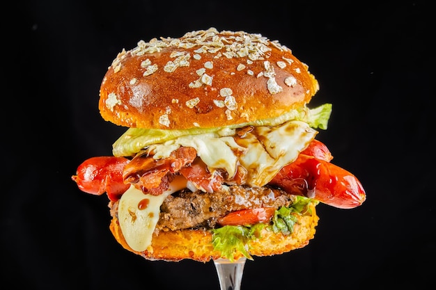 Photo gros hamburger. hamburger tourné sur fond noir foncé, avec saucisse, haut