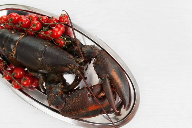 Gros homard cru dans une assiette avec des tomates sur la table avant la cuisson