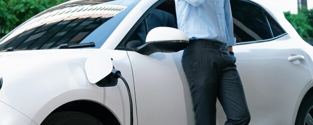 Gros homme d'affaires progressiste avec véhicule électrique à la station de charge