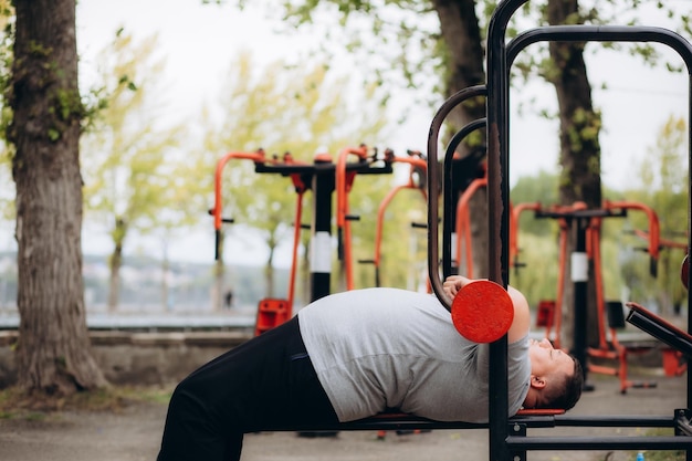 un gros homme appuie sur une barre dans le parc sur une machine d'exercice