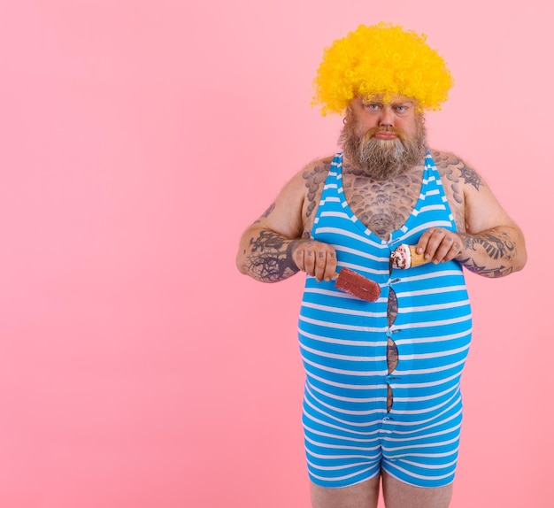 Gros homme avec barbe et perruque mange un popsicle et une glace