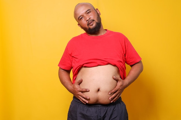 Un gros homme barbu avec un gros ventre met son ventre dehors et le touche avec ses mains.