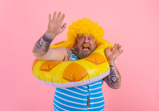 Photo un gros homme effrayé avec une perruque dans la tête est prêt à nager avec une bouée de sauvetage en beignet