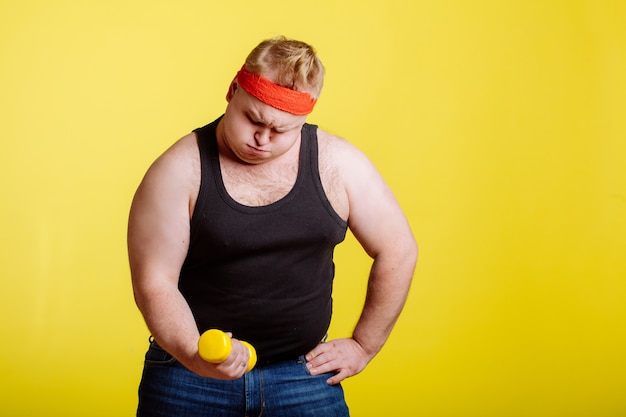 Gros homme essayant de soulever un petit haltère jaune