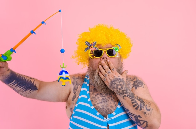 Gros homme étonné avec barbe et lunettes de soleil s'amuser avec la canne à pêche