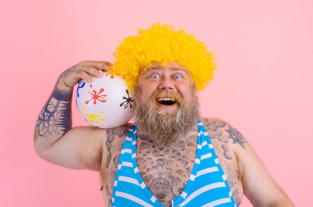 Gros homme heureux avec barbe et perruque joue avec le ballon