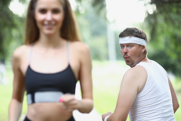 Gros homme regardant une jeune femme athlète faisant du jogging dans le parc