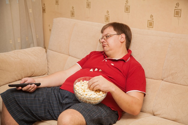 Gros homme regardant la télévision manger du pop-corn