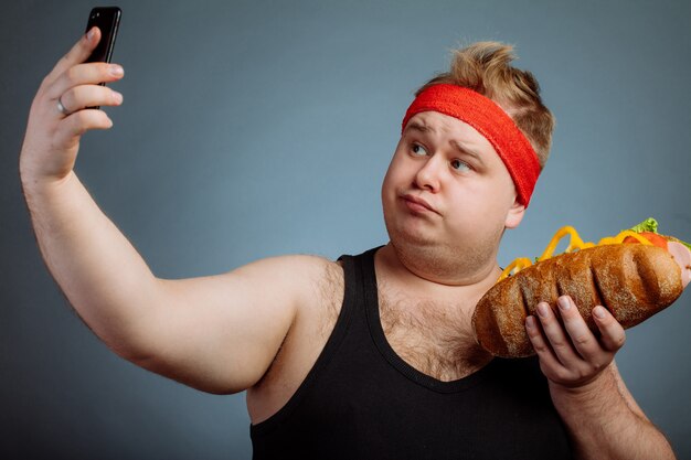 Gros homme avec sandwich à la main fait selfie