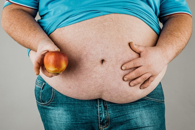 Le gros homme tient une pomme devant son estomac nu Le concept de régime alimentaire et de saine alimentation