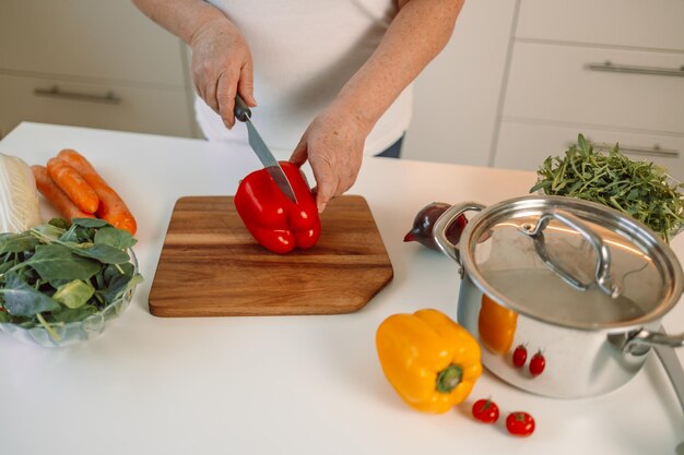 En gros, une image coupée de la planche à couper et d'une femme coupant des légumes au poivre dans la cuisine