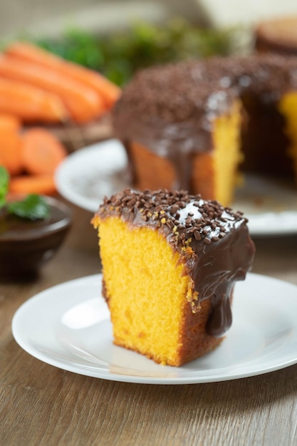 Gros morceau de gâteau aux carottes brésilien avec glaçage au chocolat sur une table en bois avec des carottes en arrière-plan