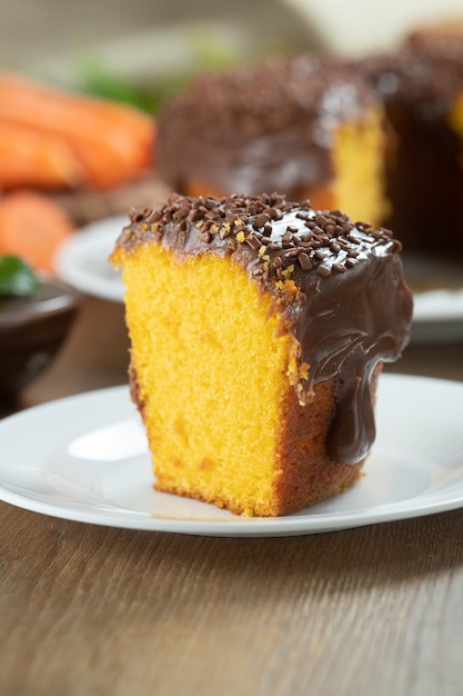 Gros morceau de gâteau aux carottes brésilien avec glaçage au chocolat sur une table en bois avec des carottes en arrière-plan