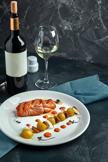 Un gros morceau de poisson rouge rôti se trouve sur une assiette blanche avec des légumes, un beau service dans un restaurant