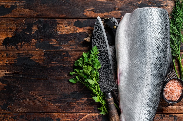 Gros morceau de poisson saumon coupé cru sur une planche à découper en bois avec couteau de chef. Fond en bois sombre. Vue de dessus. Espace de copie.