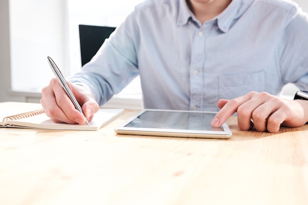 Gros plan d'un acheteur méconnaissable assis au bureau et utilisant une tablette tout en travaillant avec les médias sociaux