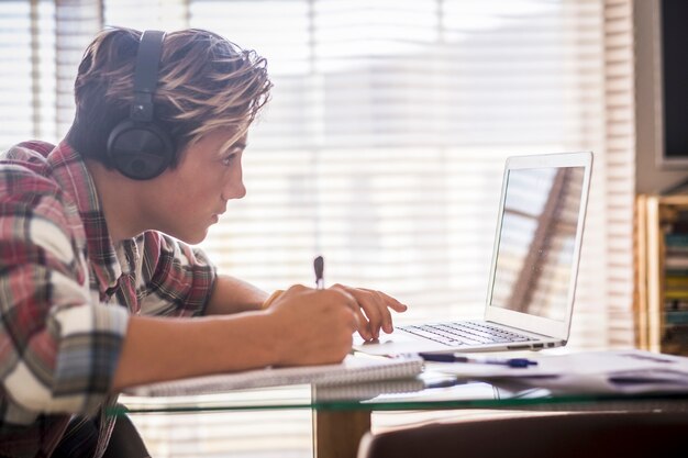 Gros plan sur un adolescent avec des écouteurs regardant l'écran d'un ordinateur portable pendant qu'il joue à des jeux informatiques, discute sur Internet ou regarde des vidéos. - Image