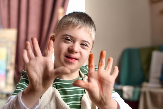 Photo en gros plan, un adolescent avec le syndrome de down montrant des mains couvertes de peinture