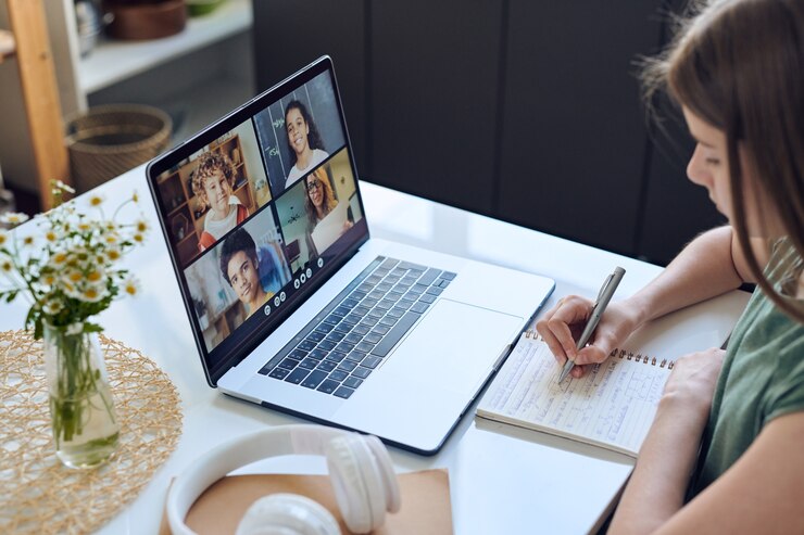 Gros plan d'une adolescente concentrée assis à table et prendre des notes tout en utilisant la plate-forme de vidéoconférence pour l'éducation en ligne