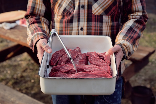 Gros plan d'un agriculteur tenant un plateau avec des tranches de viande dedans, se préparant pour un barbecue
