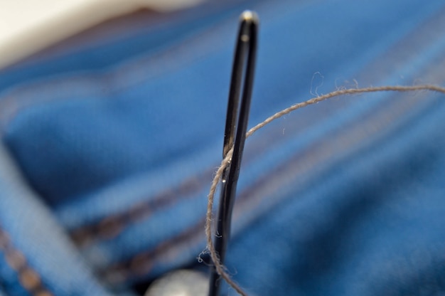 Gros plan d'une aiguille avec du fil sur un matériau de jeans. Fermer.