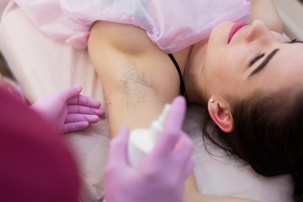 Gros plan sur l'aisselle d'une jeune fille aux cheveux, procédure d'épilation dans un salon de beauté. Esthéticienne fait shugaring aisselles pour une jeune femme. Epilation des aisselles à la pâte à sucre