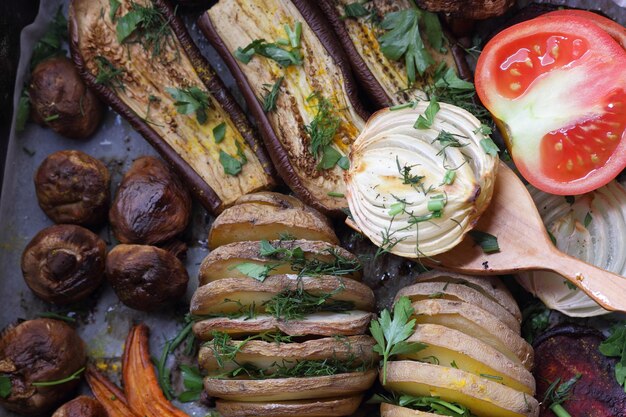 Gros plan sur des aliments sains Tranches cuites au four d'aubergines betteraves carottes oignons pommes de terre champignons entiers épices herbes et moitiés de tomates sur papier parchemin