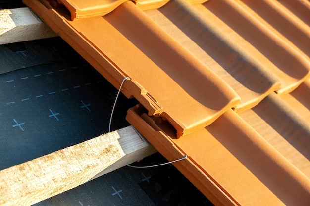 Gros plan sur une ancre de montage en métal pour l'installation de tuiles de toiture en céramique jaune montées sur des planches de bois couvrant le toit d'un bâtiment résidentiel en construction.