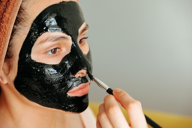 Gros plan d'une application du masque cosmétique sur le visage de la femme porte une serviette sur la tête, les soins de beauté veulent...