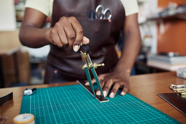 Gros plan d'une artisane noire mesurant une pièce de cuir dans un atelier de maroquinerie copie espace