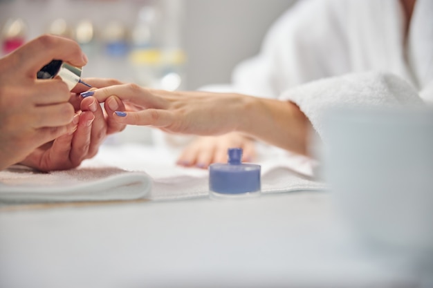 Gros plan de l'artiste couvrant les doigts féminins avec du vernis gel bleu à table in office