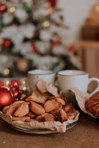 Gros plan d'une assiette avec des pâtisseries et des bonbons et des tasses blanches sont sur la table dans la cuisine de Noël