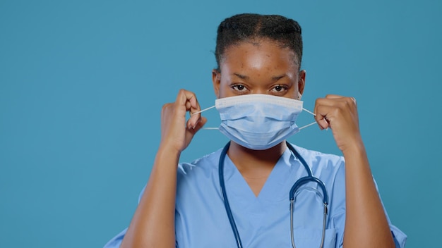 Gros plan sur un assistant médical fatigué qui enlève le masque du visage en studio. Portrait d'une infirmière se sentant épuisée tout en ayant une protection contre le coronavirus et un uniforme avec stéthoscope.