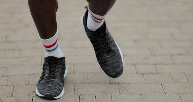 Gros plan sur un athlète afro-américain en baskets courant dans le parc, travelling. Mode de vie sain et actif.