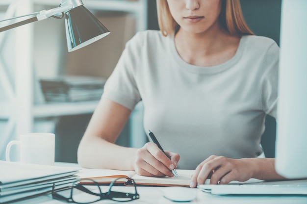 Gros plan au travail. Gros plan d'une belle jeune femme tenant la main sur le menton et regardant la caméra alors qu'elle était assise sur son lieu de travail au bureau