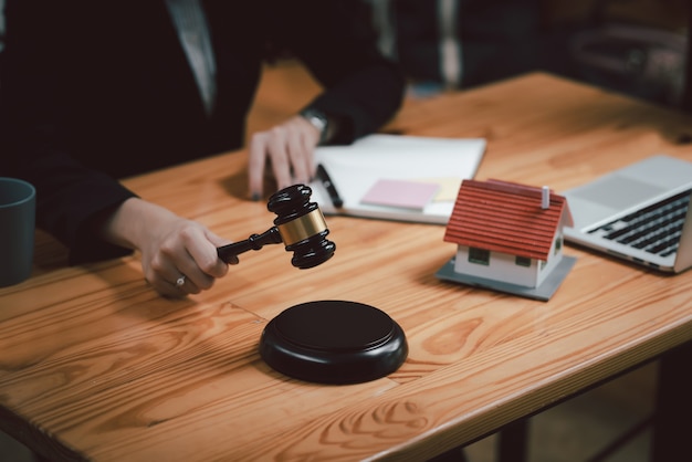 Photo gros plan d'une avocate tenant un maillet avec un ordinateur portable de maison modèle placé au bureau.