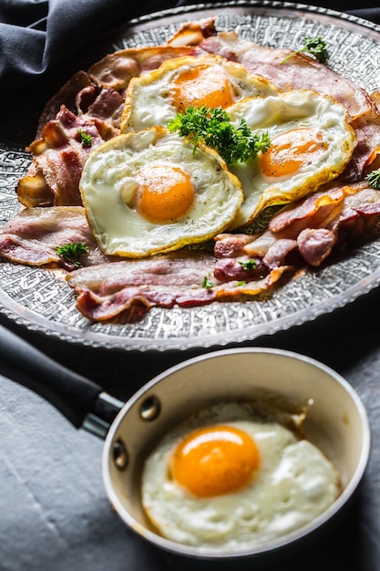 Gros plan de bacon rôti et d'œufs aux herbes sur une assiette.