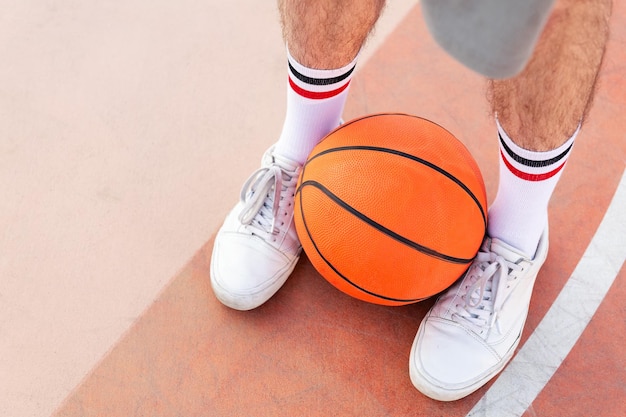 Photo gros plan d'un ballon tenu entre les pieds d'un homme sur un terrain de basket concept de sport urbain dans l'espace de copie de rue pour le texte