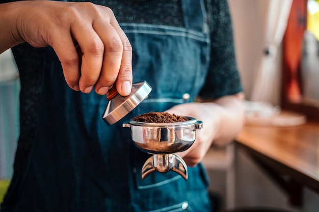 Gros plan d'un barista à la main ou d'une cafetière tenant un porte-filtre et un bourreur de café faisant un expresso