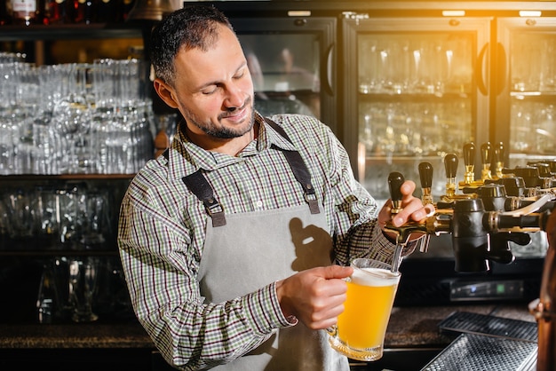 Gros plan d'un barman barbu remplissant une chope de bière blonde. Le comptoir du bar dans le pub.