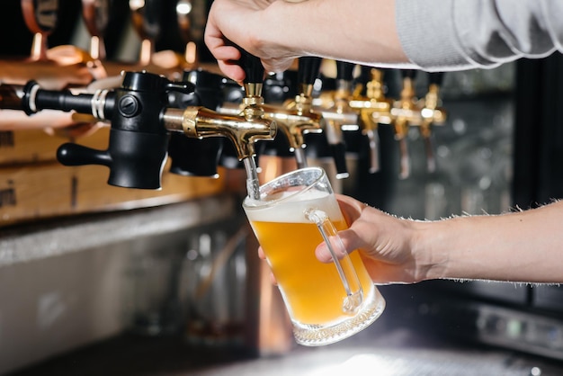 Gros plan sur le barman remplissant une chope de bière légère. Le comptoir du bar dans le pub.