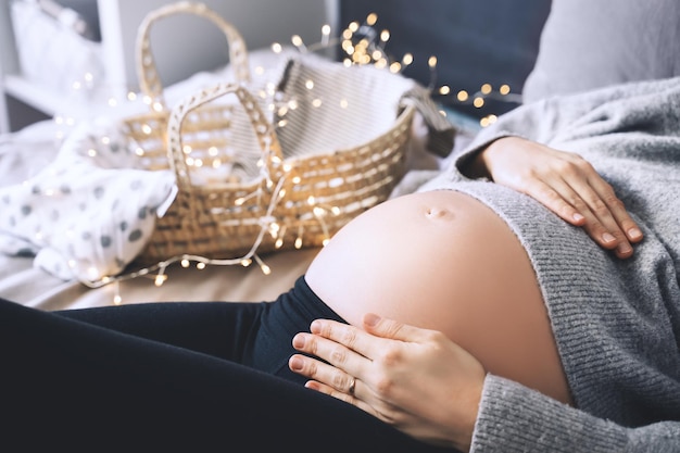 Gros plan beau ventre de femme enceinte en pull tricoté à la lumière des guirlandes