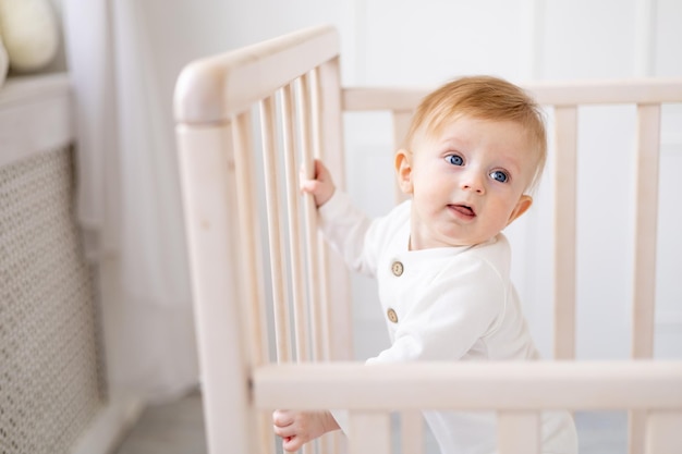 Gros plan d'un bébé souriant de 6 mois garçon blond dans un berceau dans une chambre lumineuse dans un concept de portrait de body en coton blanc de produits pour enfants