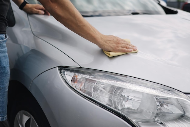 Gros plan d'un bel homme essuie une voiture avec un chiffon dans une salle d'exposition lors d'un lavage de voiture en libre-service voiture grise retour