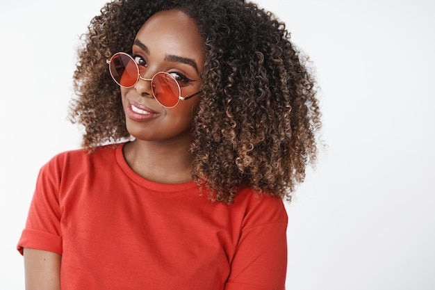 Gros plan d'une belle femme afro-américaine séduisante et sensuelle dans des lunettes de soleil élégantes inclinant la tête et regardant amusé