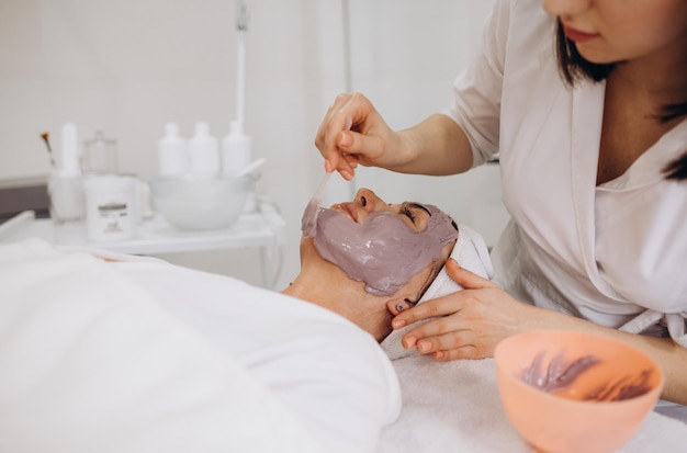 Gros plan d'une belle femme allongée les yeux fermés et cosmétologue appliquant un masque facial