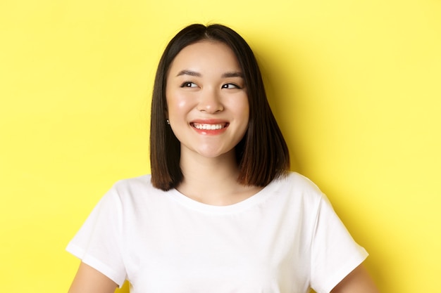 Gros plan d'une belle femme asiatique en t-shirt blanc, souriant et regardant à gauche avec un visage heureux