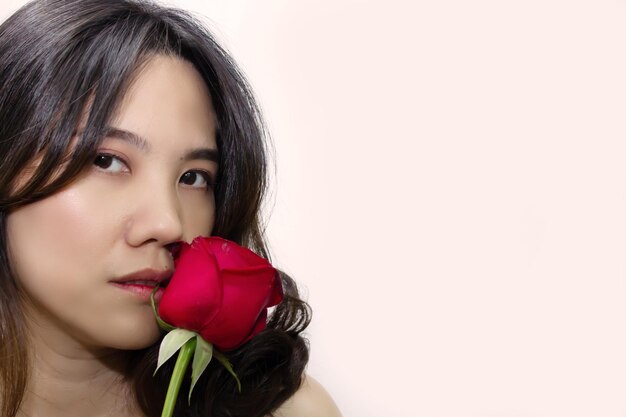 Gros plan belle femme asiatique tient une rose rouge à côté de la bouche Saint Valentin et amour