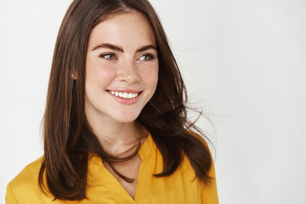 Gros plan d'une belle femme debout près du logo sur un mur blanc, souriant et regardant à droite