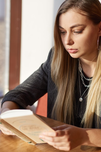 Photo gros plan d'une belle femme en vêtements noirs lisant un livre assis dans un café